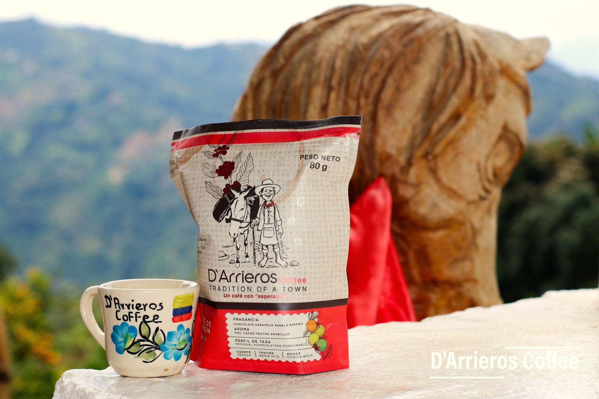 Bolsa de café D'Arrieros y una taza pintada a mano frente a las montañas de Palmitas